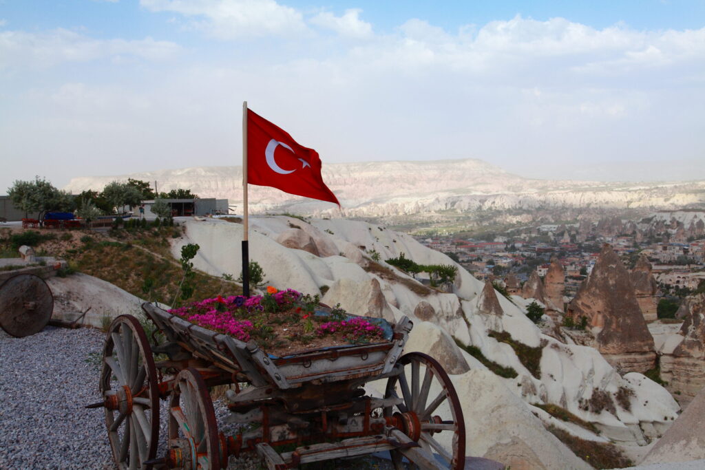 トルコ・カッパドキアの丘の上に立つトルコ国旗。壮大な奇岩群と歴史ある街並みが広がる絶景。